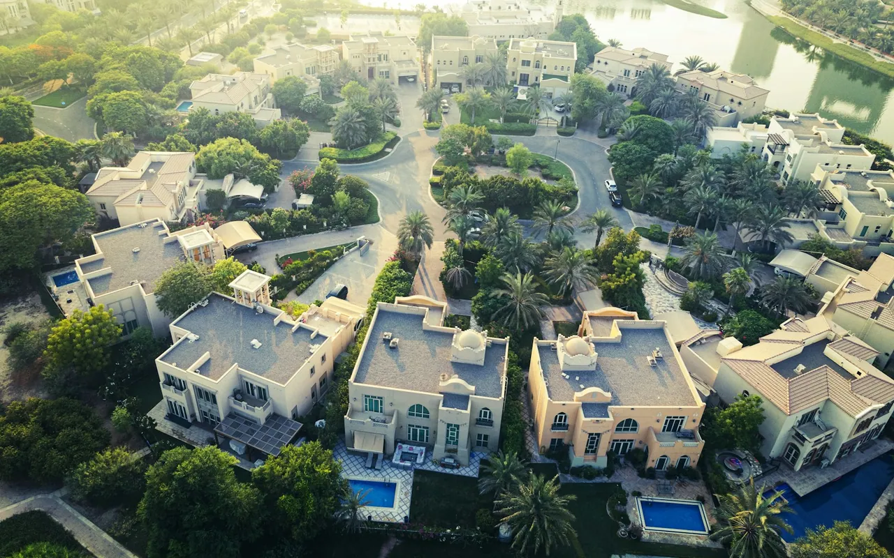 Aerial photograph of landscaped Dubai villas, private pools and lakeside gardens — representative Dubai photograph, not a view of The Meadows