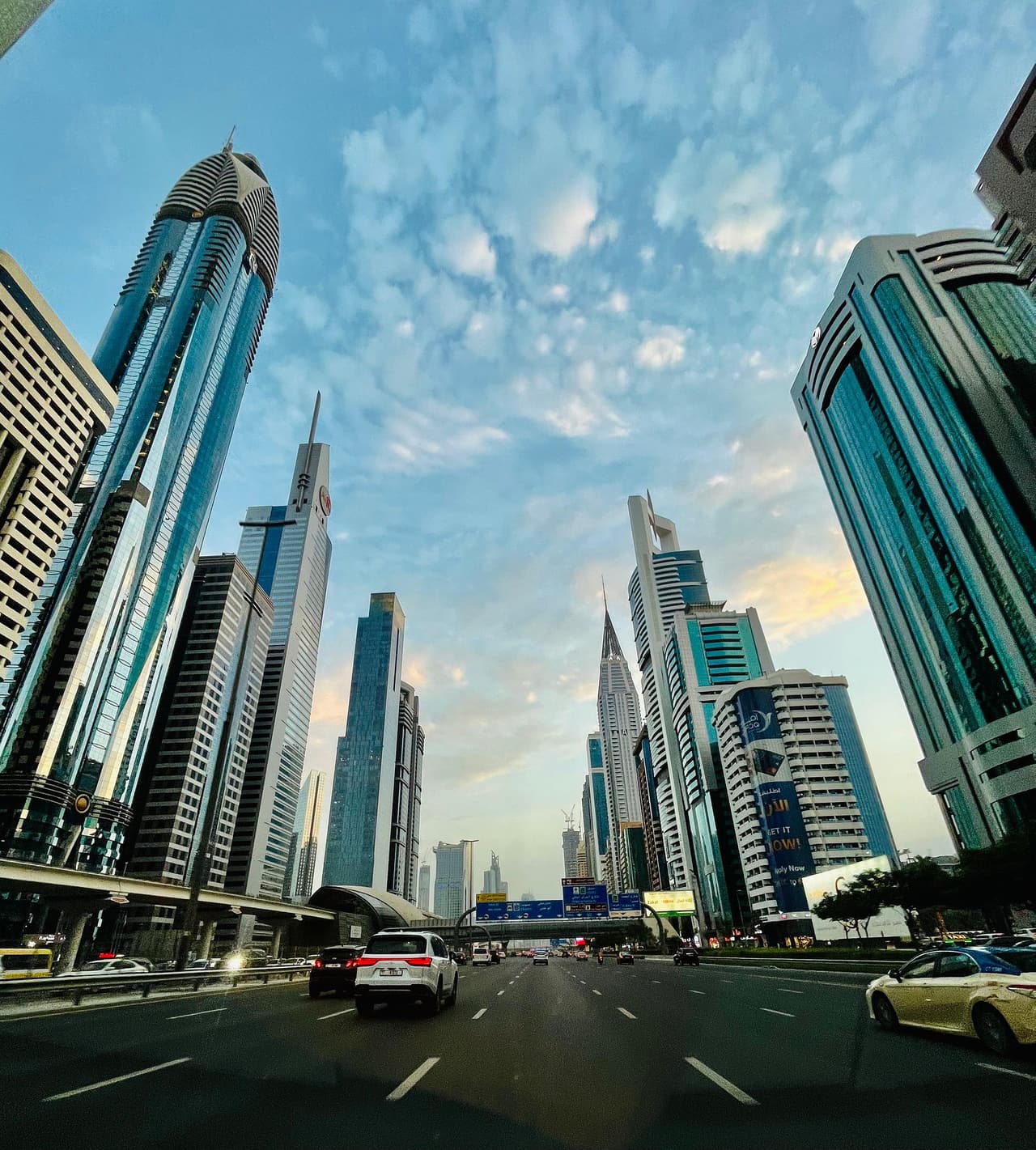 High-rise towers on both sides of a multi-lane road in Dubai, seen from street level